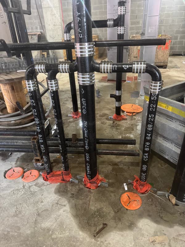 Cast-iron no-hub drainage risers and horizontal branch joined with banded shielded couplings, stub-ups capped in orange mesh