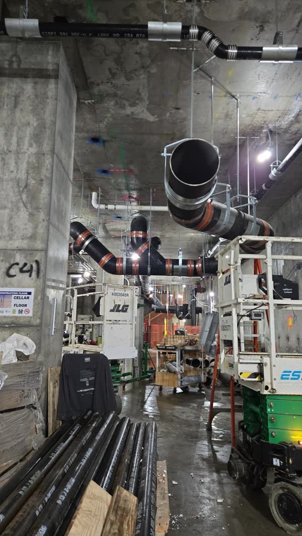 Overhead cast-iron no-hub main with wye fittings and banded shield couplings running the length of a cellar corridor