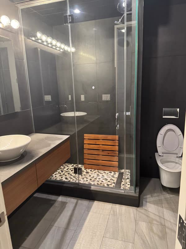 Finished dark-tile bathroom with glass shower enclosure, pebble shower floor, floating walnut vanity and wall-hung toilet