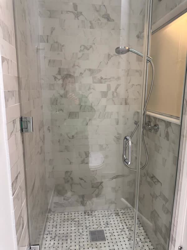 Finished marble-tiled shower with frameless glass door, chrome slide-bar handshower, thermostatic valve and basketweave…