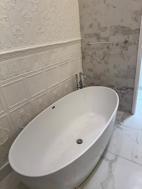 White freestanding oval soaking tub with chrome floor-mounted tub filler against pressed-tin wall panelling and marble tile