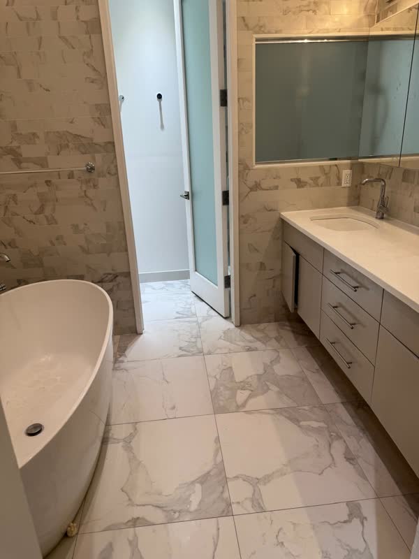 Finished bathroom with freestanding tub, marble-tiled walls and floor, and a long vanity with undermount sink and chrome…