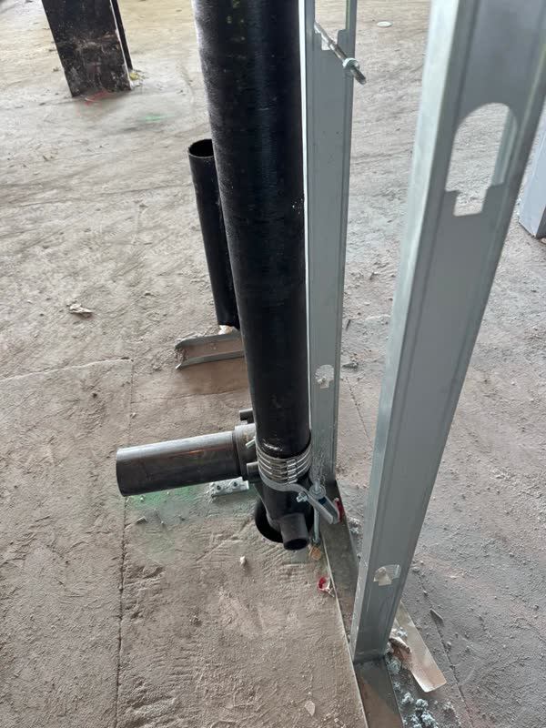 Close-up of a stainless no-hub band coupling joining a cast-iron stack to a capped branch fitting, clamped to a steel stud