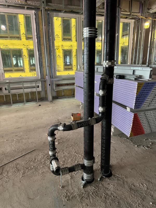 Two cast-iron no-hub stacks anchored to a concrete floor with a banded elbow and trap arm offset