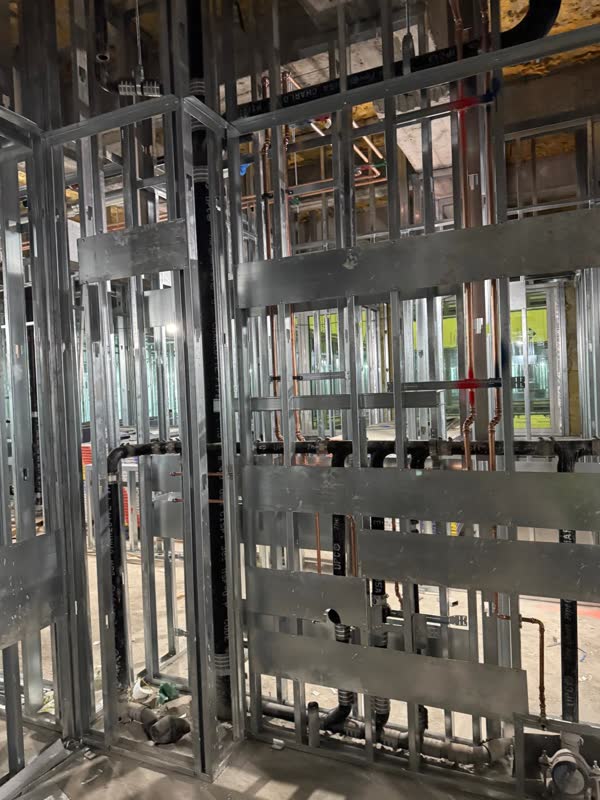 Copper hot and cold branch lines and a cast-iron stack roughed into steel-stud framing with backing plates