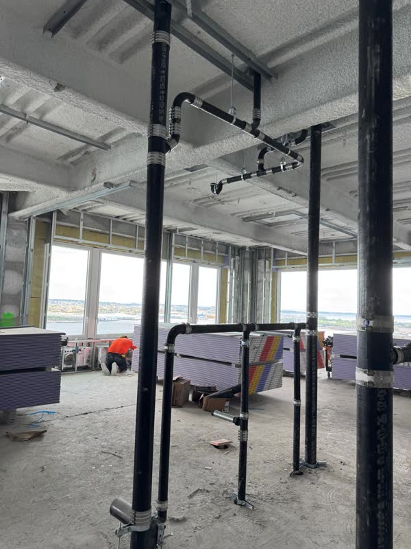 Cast-iron no-hub risers and an overhead waste branch banded to a concrete deck on a high-rise floor